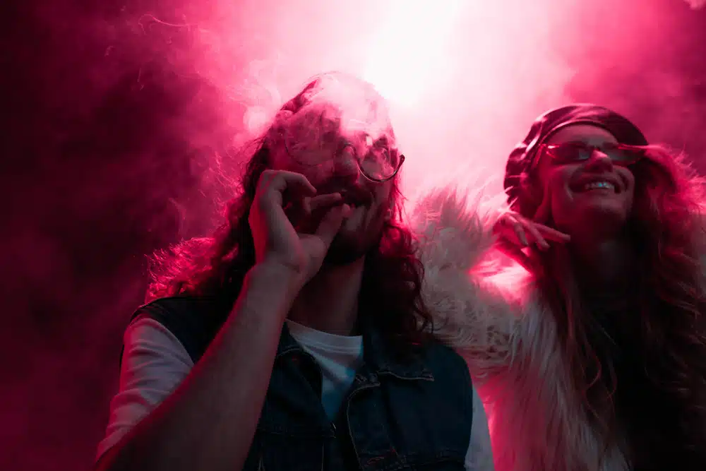 man smoking marijuana joint near smiling girl in nightclub