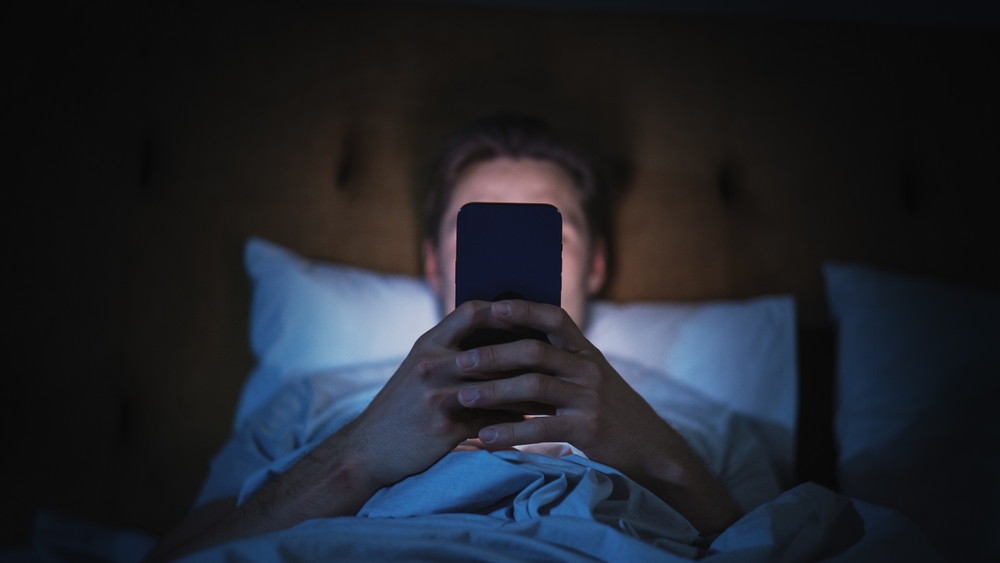 Man in bed at night dealing with mental repercussions from excessive screen time considering digital detox