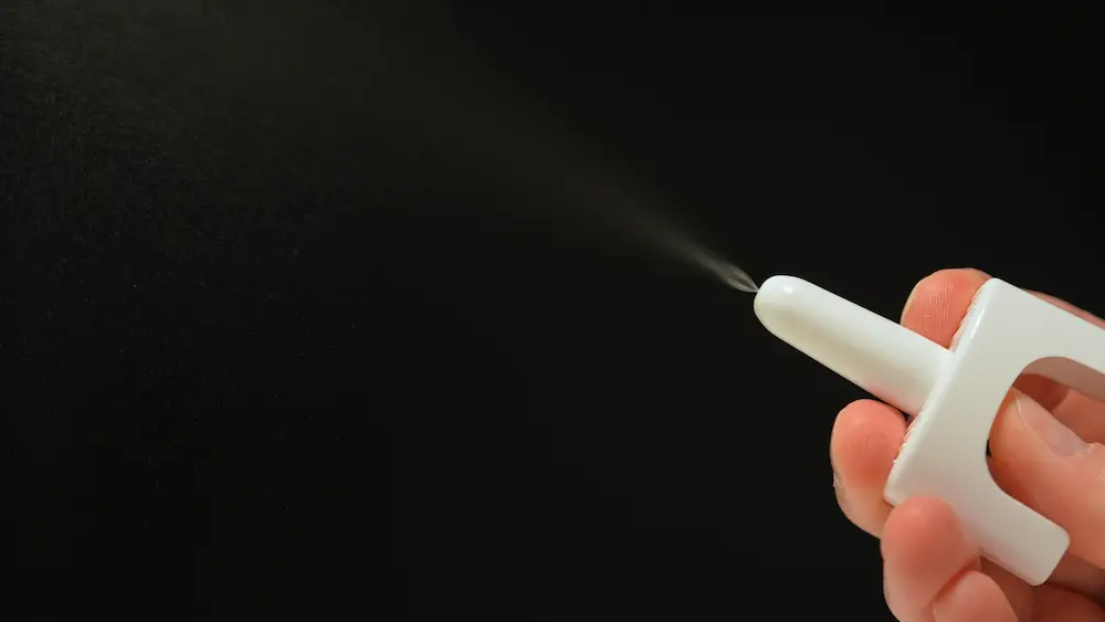 A close-up of a hand pressing a white nasal spray device, releasing a fine mist against a black background. This represents naloxone (often known by the brand name Narcan), which is highlighted as an essential, life-saving reversal agent for tianeptine overdoses.
