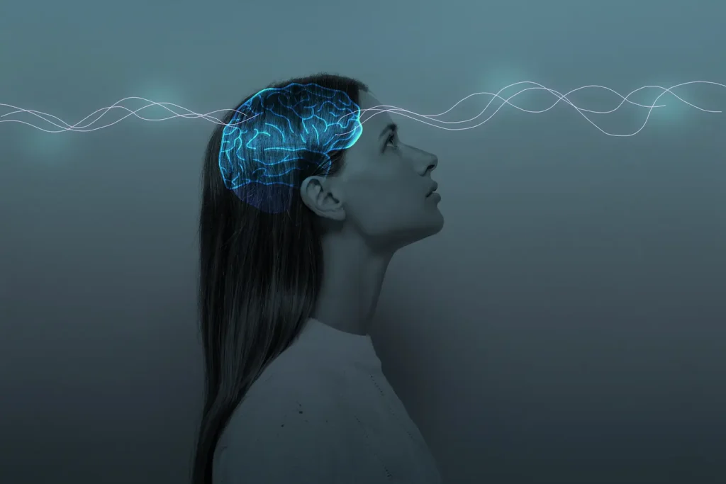 a conceptual illustration features the side profile of a woman looking upward against a dark, grey-blue gradient background. Superimposed over her head is a glowing, translucent blue graphic of a human brain. Thin, luminous, wavy lines pass horizontally across the image and directly through the glowing brain, suggesting brainwaves, signals, or neurological activity.